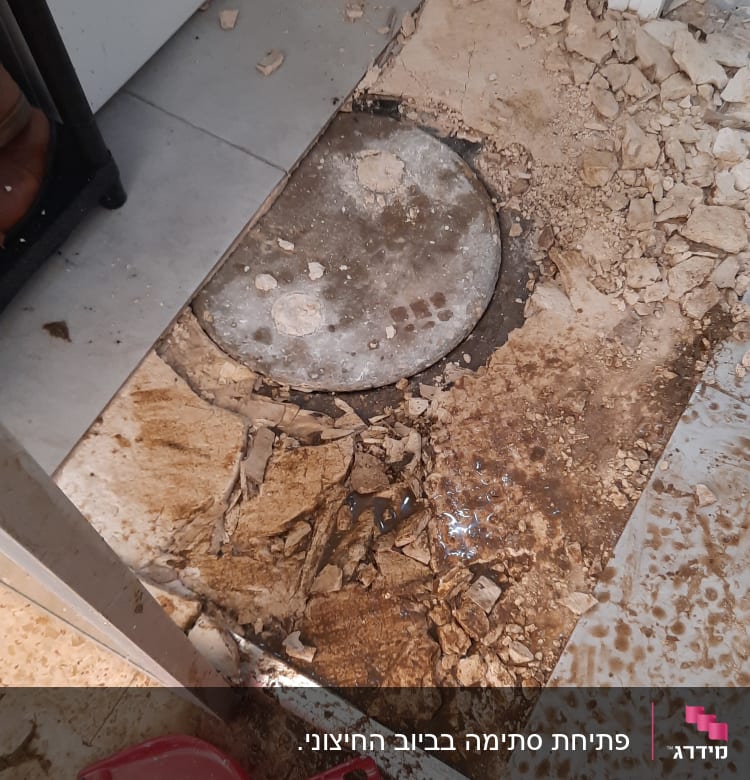 פתח ביוב פתוח עם שברים ופסולת סביב